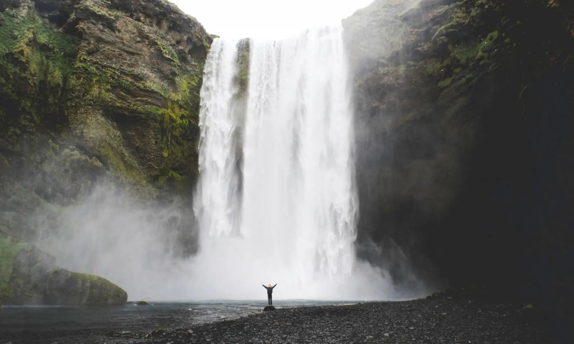 A huge waterfall in the background and a small figure standing at the bottom, raising their arms.